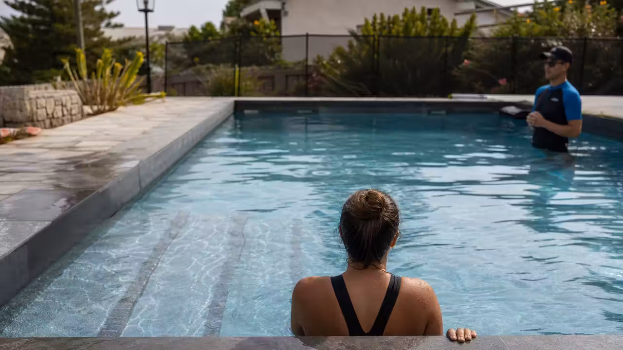 Adulte débutant accompagné près des marches d’une piscine privée sécurisée et bordée d’une terrasse.