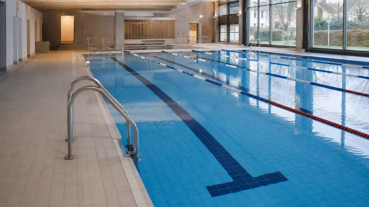 Bassin intérieur rénové d’une piscine municipale avec lignes d’eau, plages claires et baies vitrées