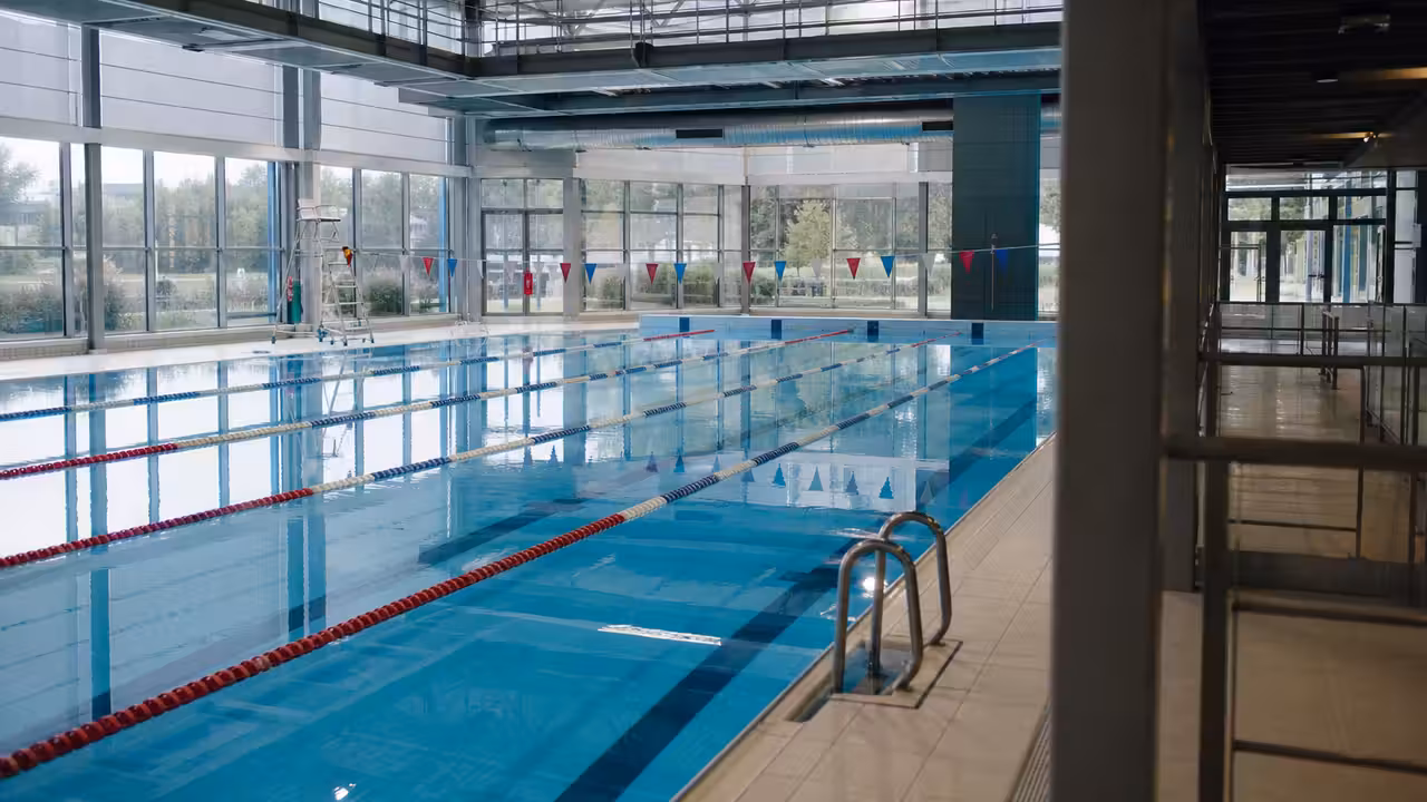 Halle de bassin municipale vide avec coursive sécurisée, plafond entretenu et lignes d’eau calmes