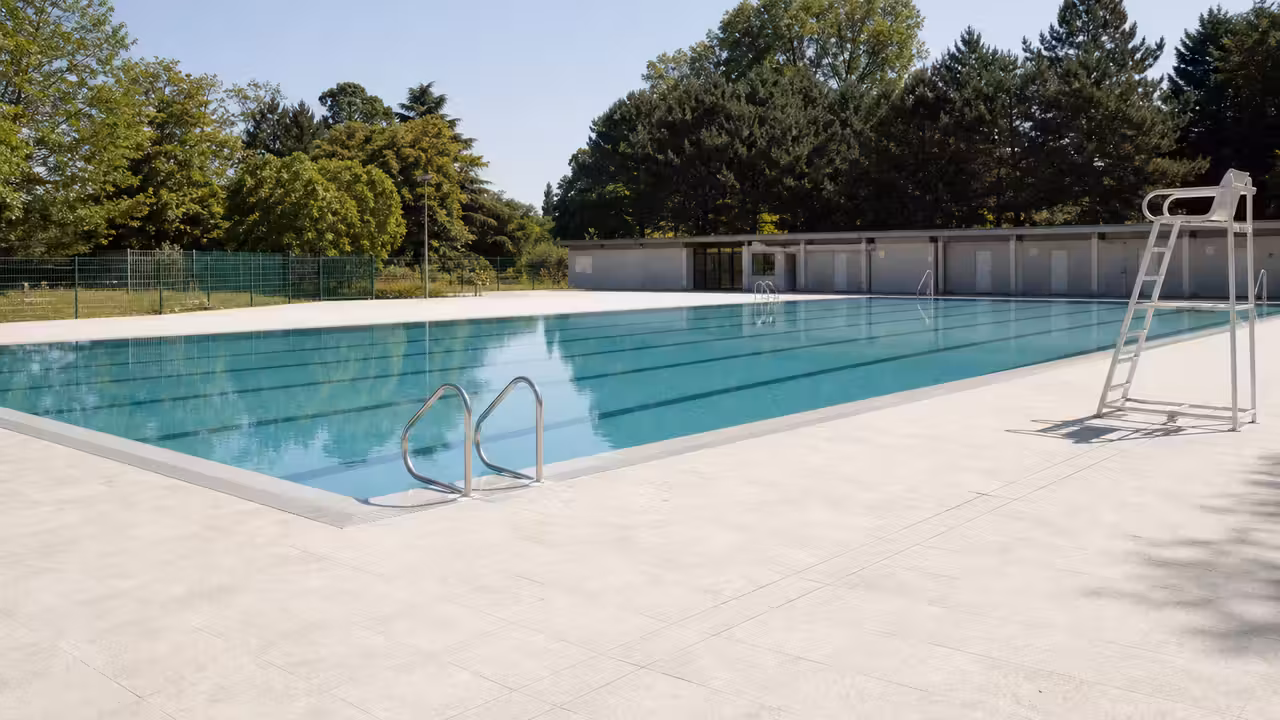 Piscine municipale extérieure avec bassin de nage, plages minérales et vestiaires en arrière-plan