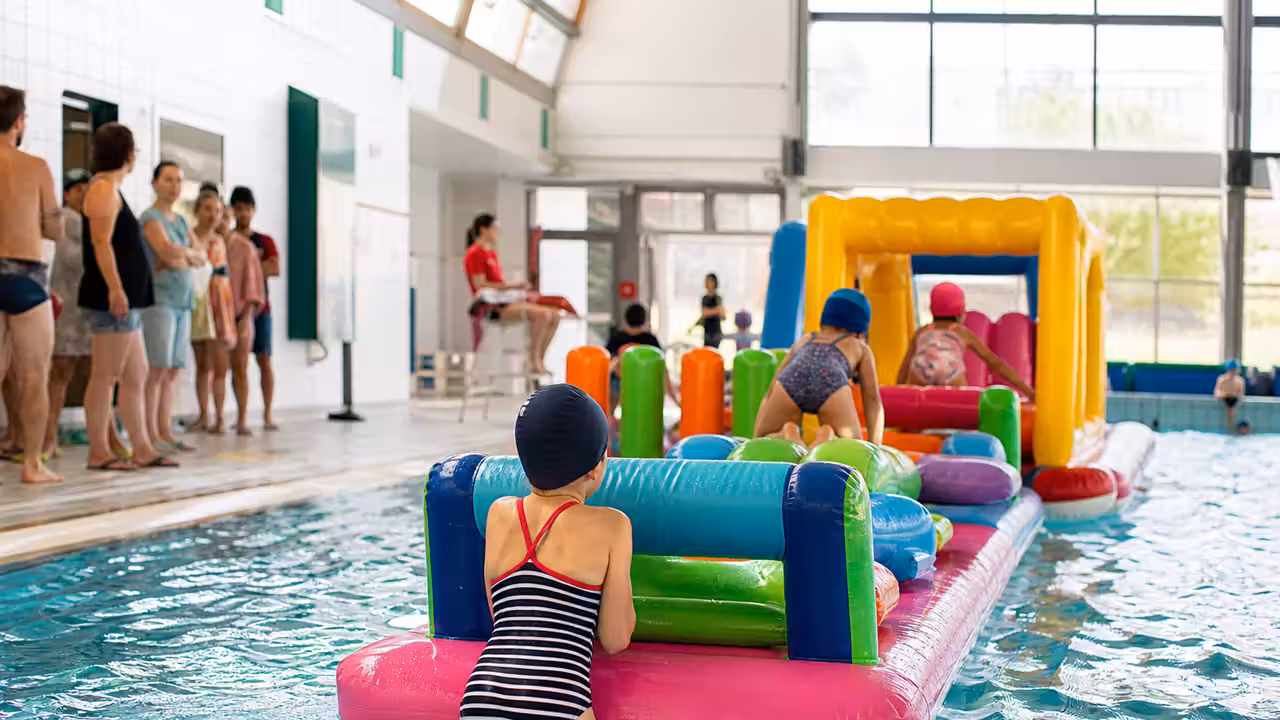 Jeux aquatiques installés dans un bassin municipal, sous la surveillance d’adultes au bord de l’eau