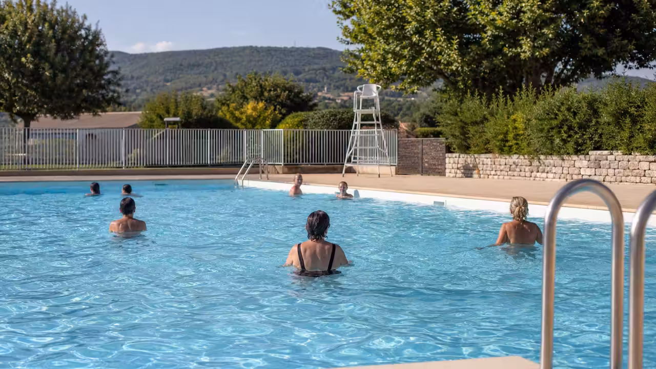 Bassin municipal en plein été avec baigneurs adultes, maître-nageur et espaces de détente autour de l’eau