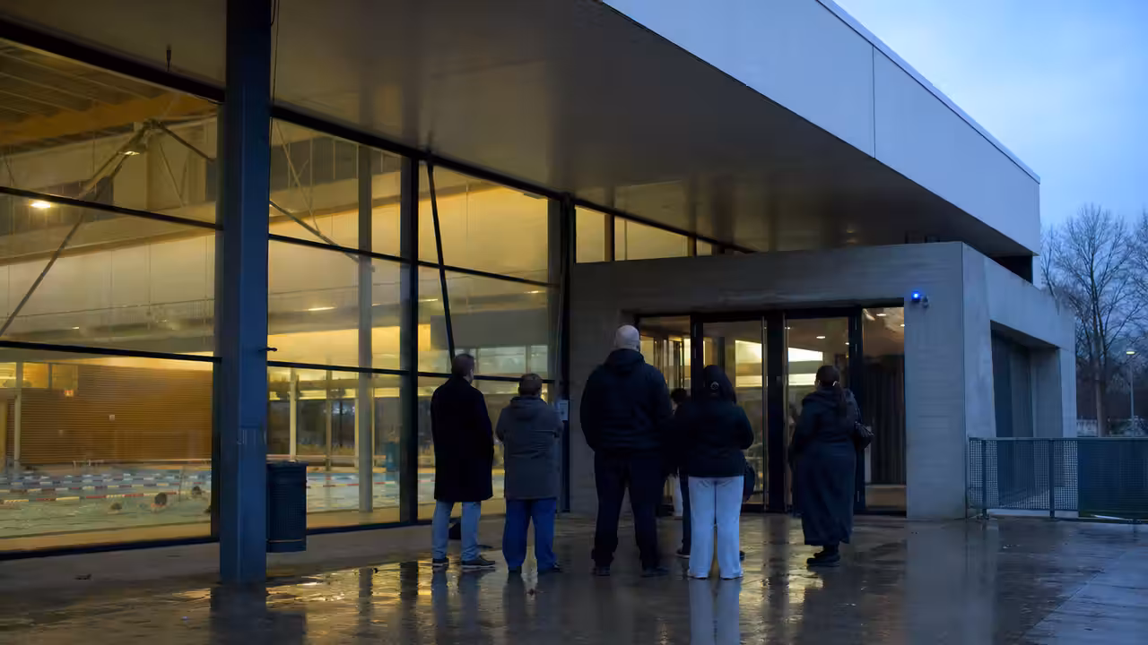 Usagers attendant tôt le matin devant l’entrée vitrée d’un centre aquatique municipal en Loire