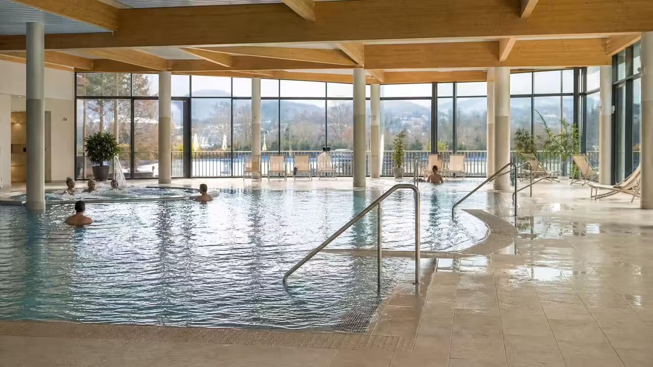 Intérieur lumineux d’un centre aquatique rénové avec bassin de loisirs, plages minérales et baies vitrées