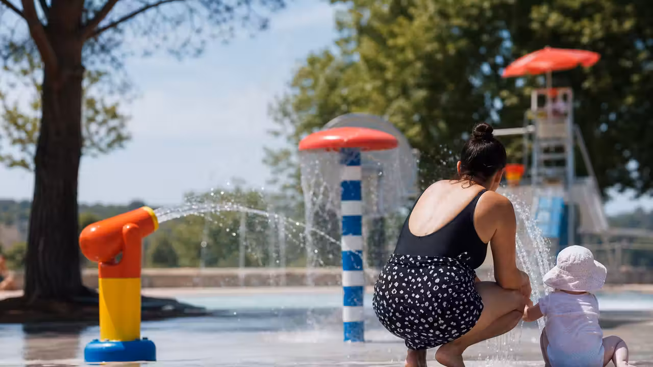 Jeune enfant accompagné par un adulte dans une aire de jeux d’eau avec jets et sol antidérapant