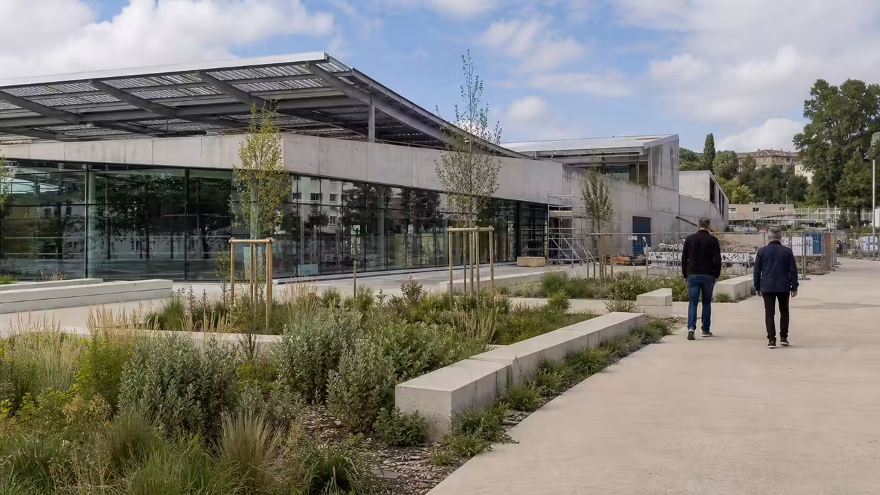 Bâtiment de piscine municipale contemporain avec toiture mobile, baies vitrées et parvis paysager.