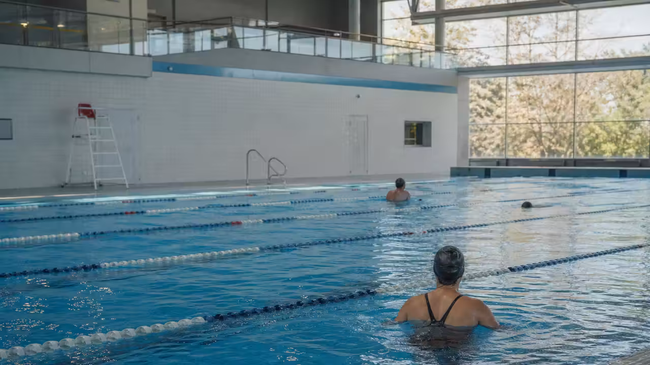 Bassin couvert d'une piscine publique avec lignes d'eau et baigneurs vus de dos un jour férié