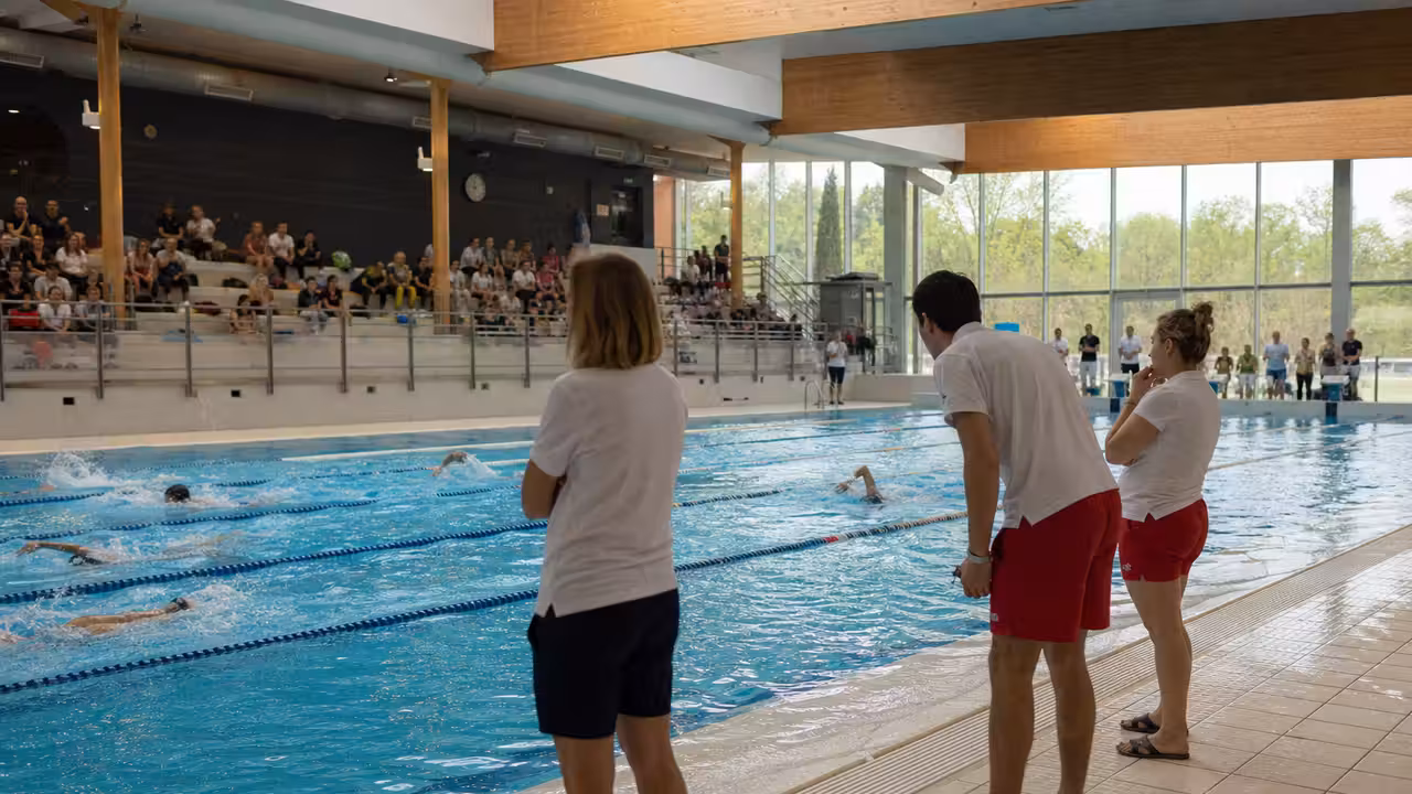 Élèves encadrés lors d’un relais de natation dans un bassin couvert de piscine publique