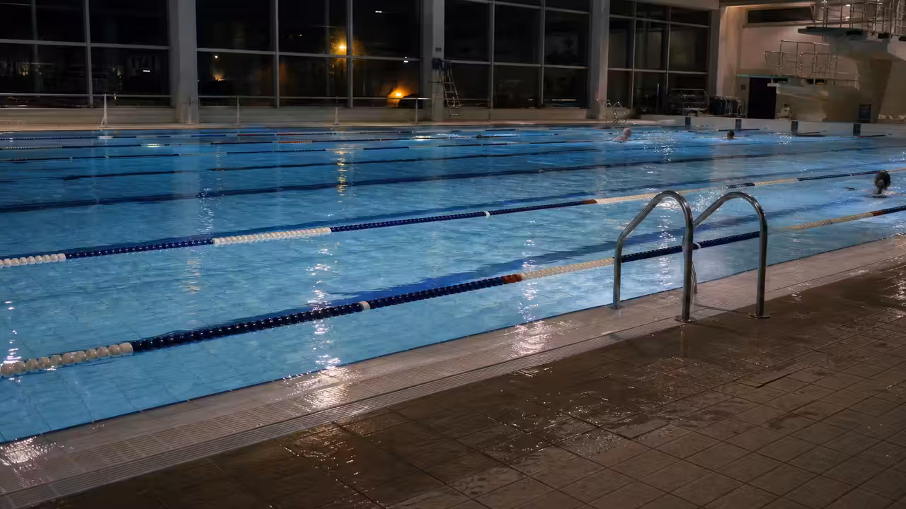 Bassin intérieur de piscine publique éclairé doucement lors d’une séance nocturne, avec couloirs visibles