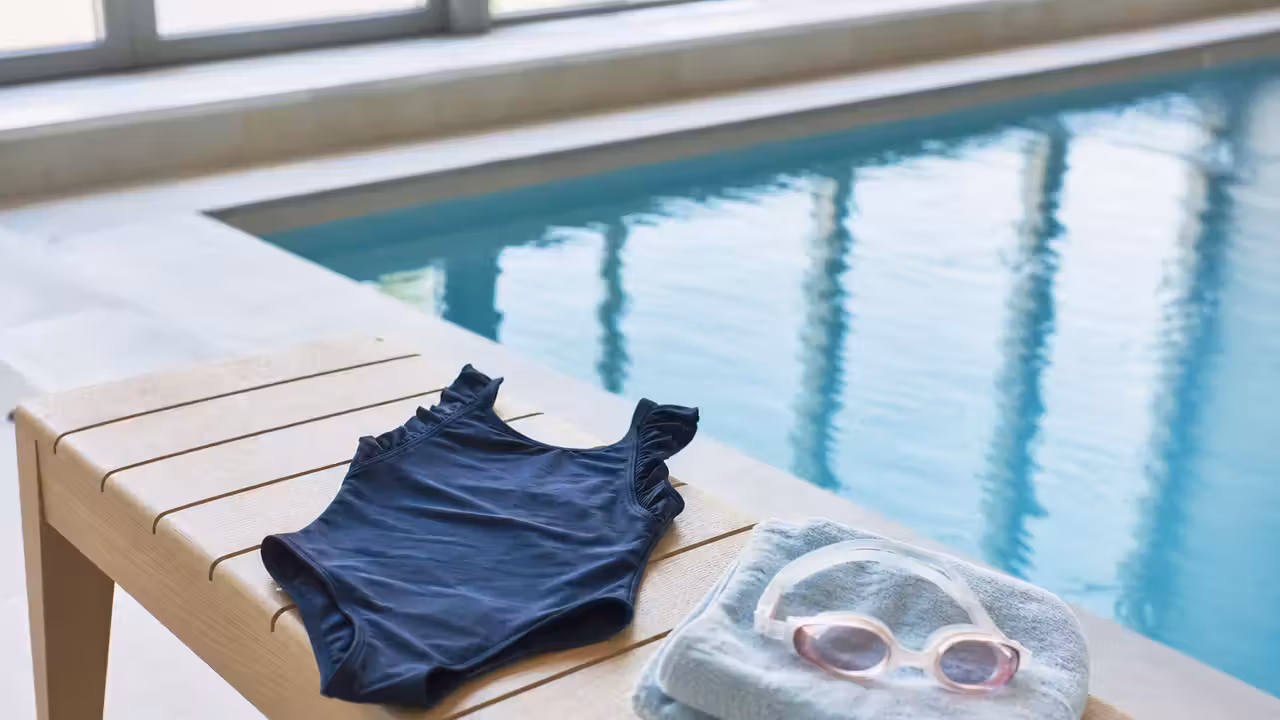 Maillot une pièce bleu marine pour enfant séchant sur un banc près d'un bassin couvert