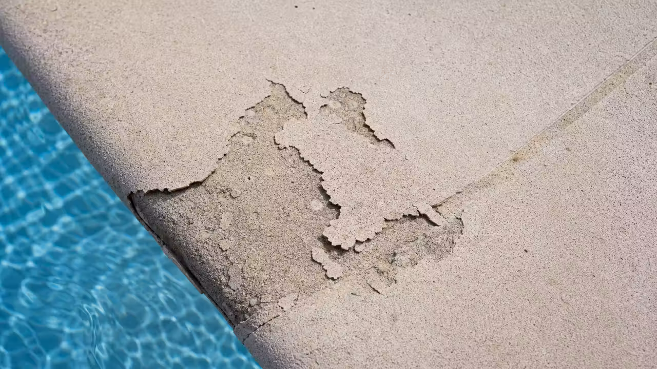 Margelle de piscine avec une zone de revêtement cloquée et fissurée révélant le support en dessous