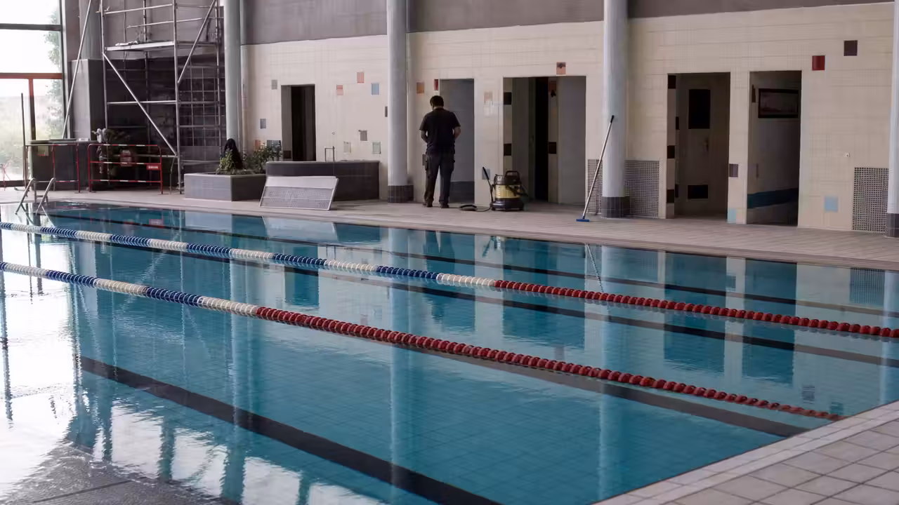 Vestiaires vides d’une piscine municipale fermée, avec casiers, bancs carrelés et accès au bassin en arrière-plan