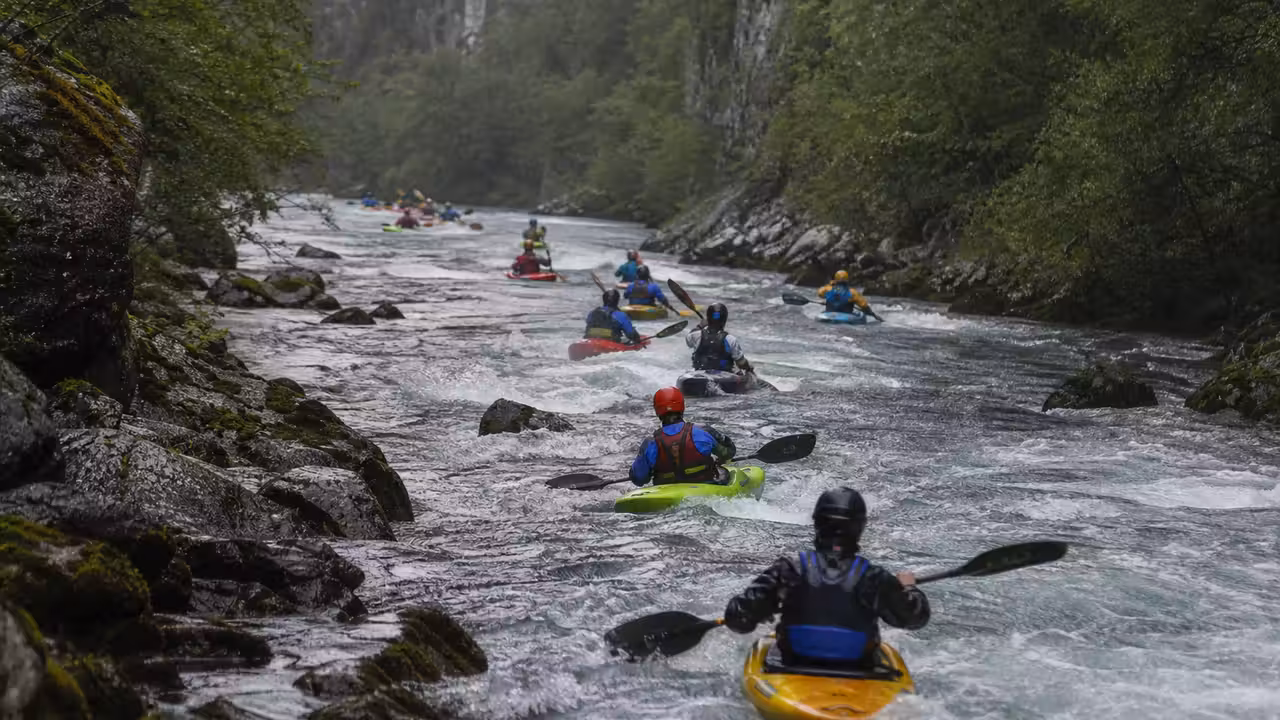 Kayakistes casqués progressant en groupe sur une rivière encaissée sous une pluie légère