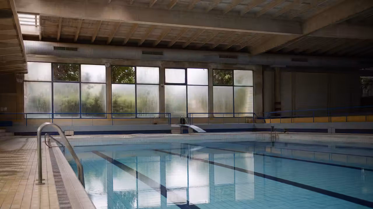 Bassin intérieur d’une piscine municipale avec lignes d’eau et structure architecturale des années 1970