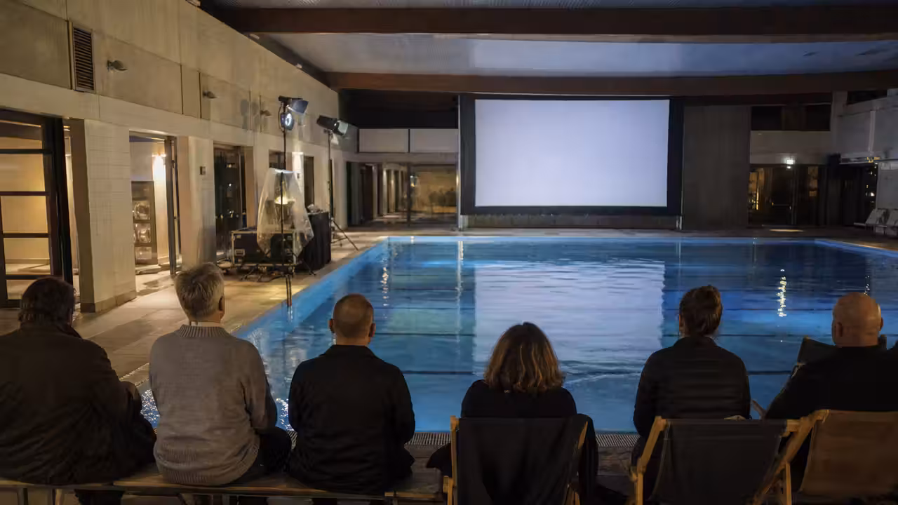 Projection de cinéma installée au bord d’un bassin intérieur avec spectateurs assis sur les plages.