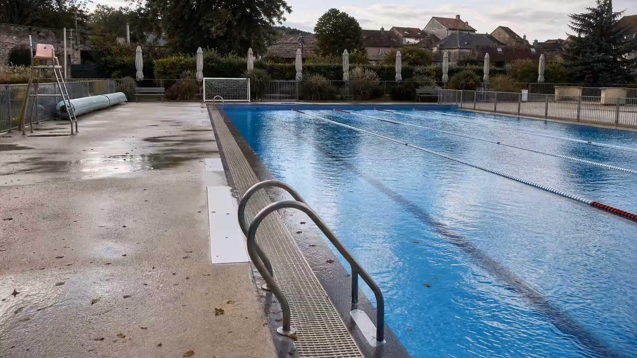 Bassin extérieur municipal vide en fin de saison, bordé de plages minérales et de végétation