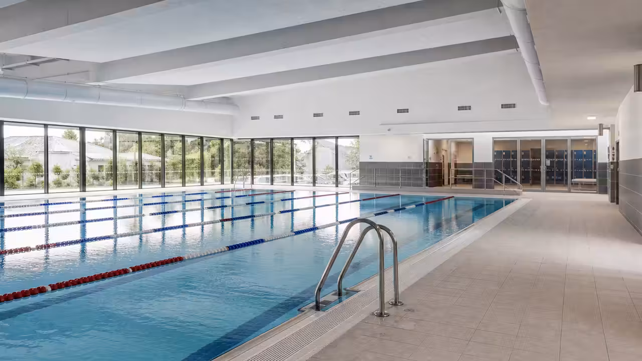 Bassin intérieur rénové d’une piscine municipale avec baies vitrées, lignes d’eau et plages antidérapantes