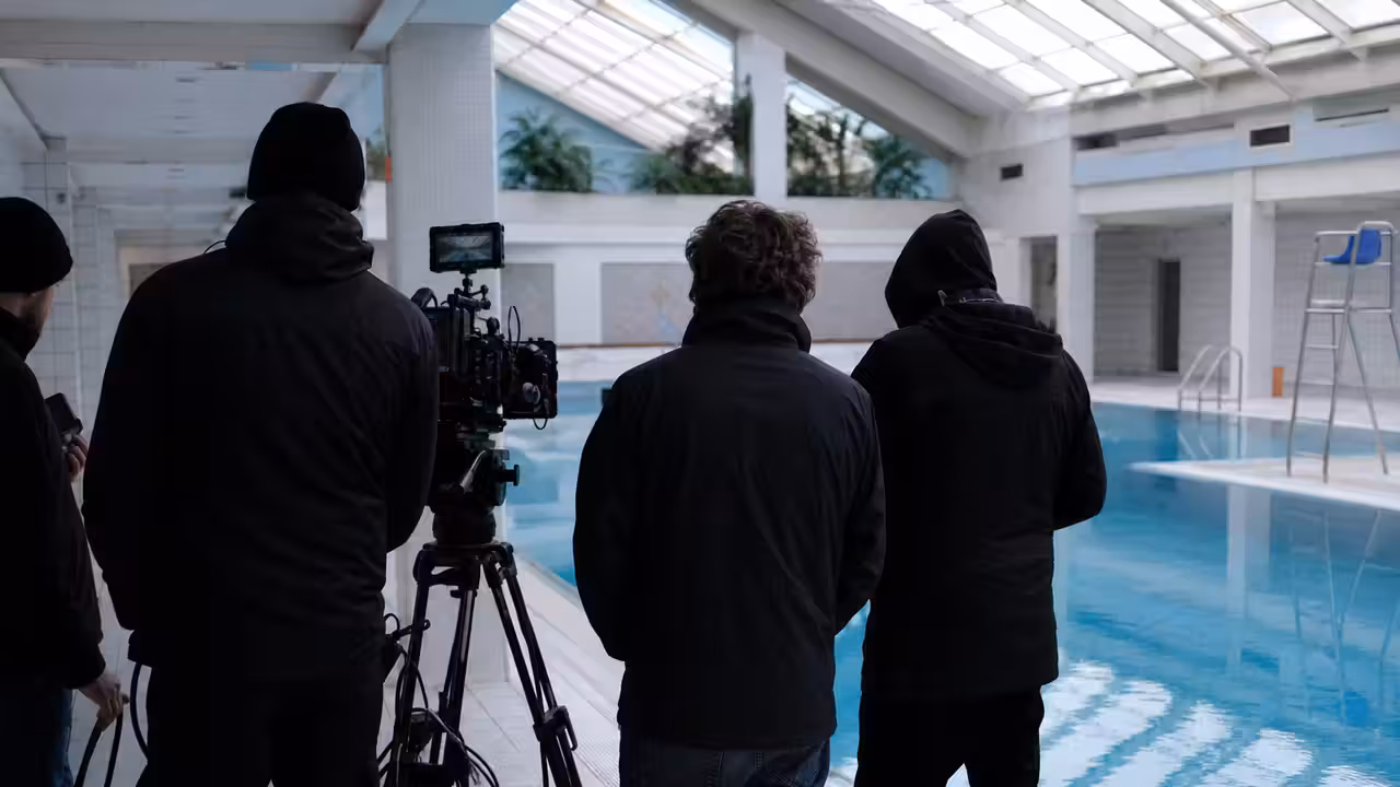 Équipe de tournage installant discrètement une caméra au bord d’un bassin couvert sans baigneurs visibles