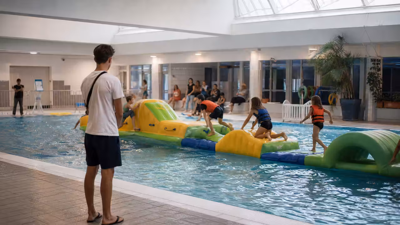 Enfants vus de dos participant à un parcours gonflable sous la surveillance d’un maître-nageur en piscine