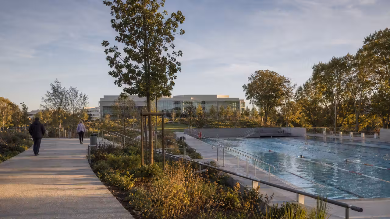 Vue paysagère d’un parc urbain avec bassin de natation extérieur et bâtiments publics en arrière-plan