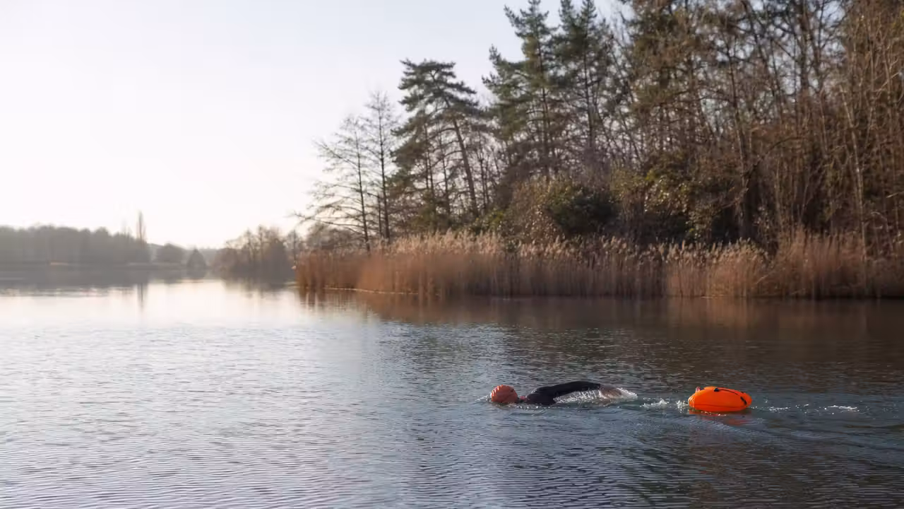 Nageur équipé d’une bouée orange progressant près du rivage sur un lac calme au lever du jour
