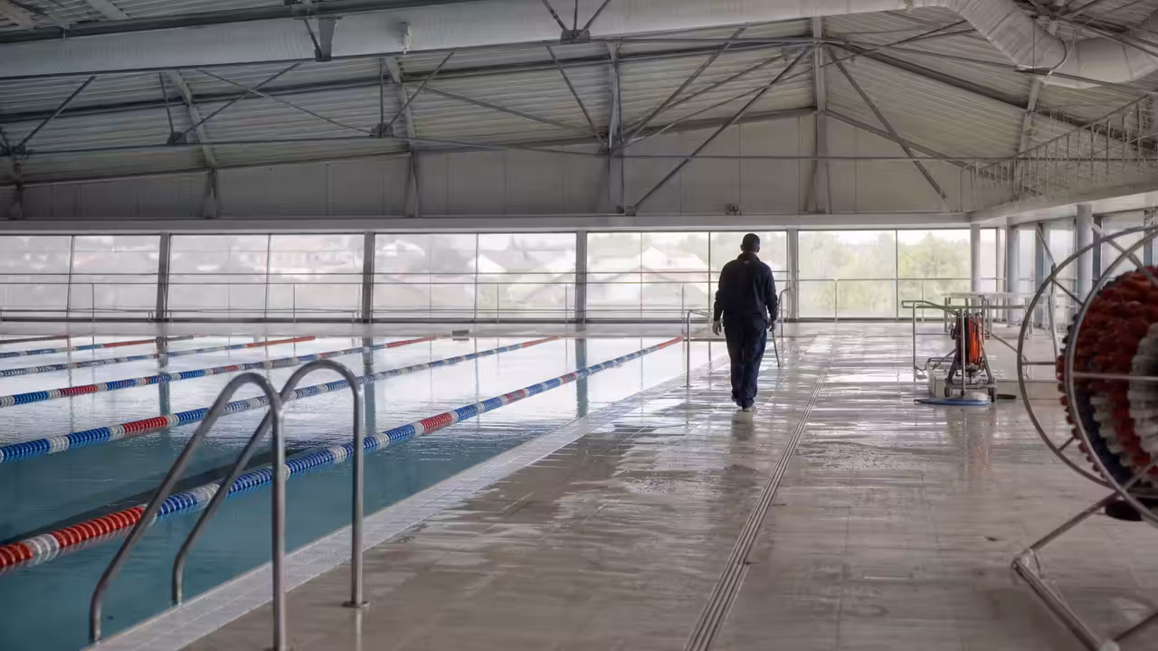 Bassin sportif couvert de 25 mètres vide, lignes d’eau et charpente métallique visibles à Narbonne