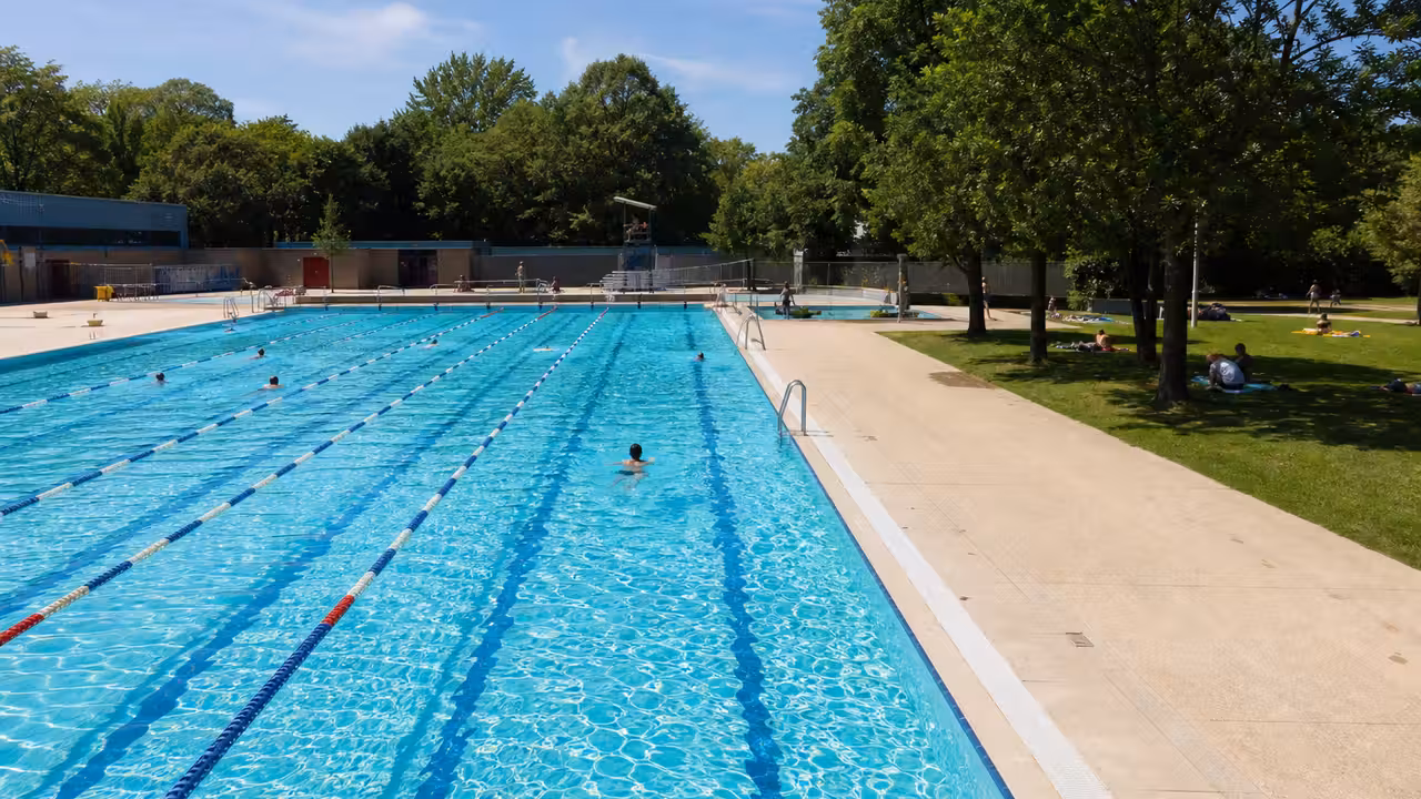 Bassin extérieur de 25 mètres bordé de pelouses et d’arbres dans une piscine municipale estivale