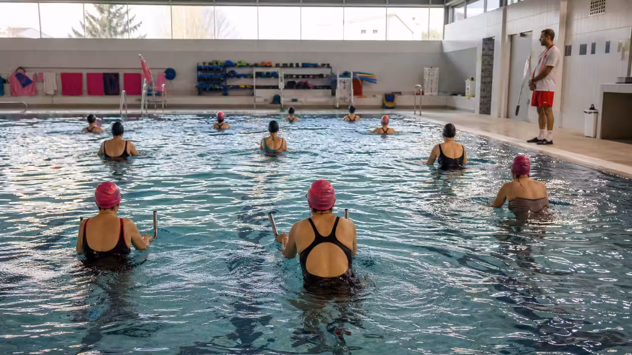 Participants adultes vus de dos lors d’une animation aquatique solidaire dans une piscine couverte aux touches roses