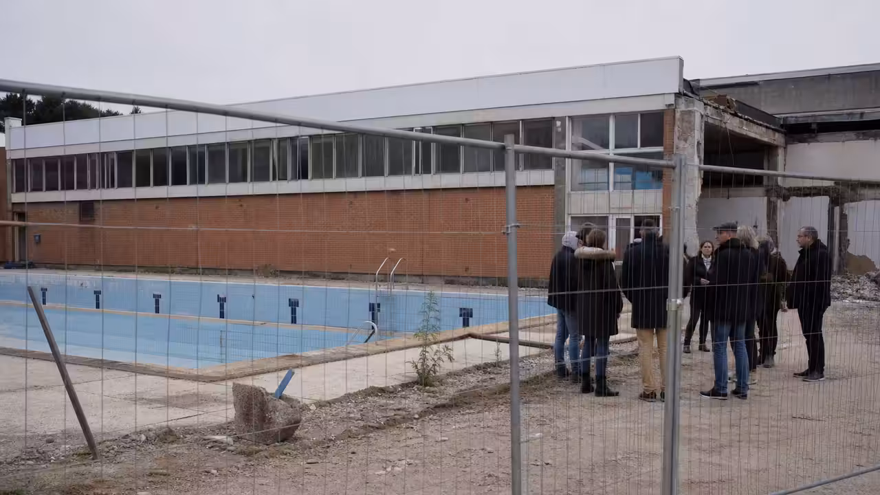 Bâtiment de piscine publique ancien derrière une clôture de chantier, avec bassin vide en arrière-plan