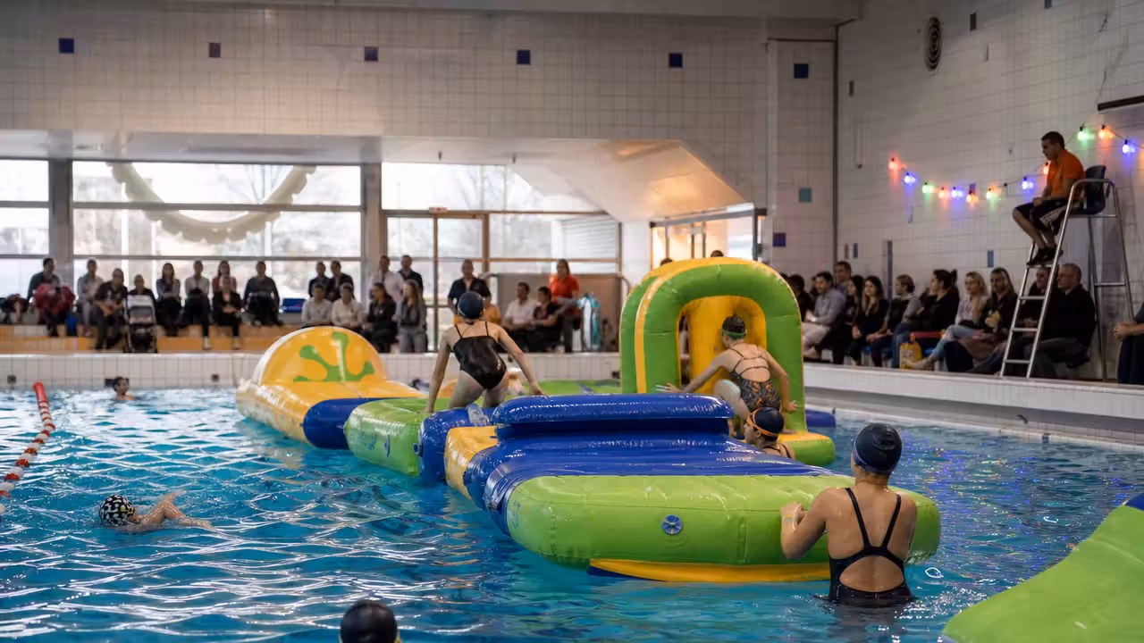 Animation aquatique festive dans une piscine municipale, avec structure gonflable et familles au bord du bassin