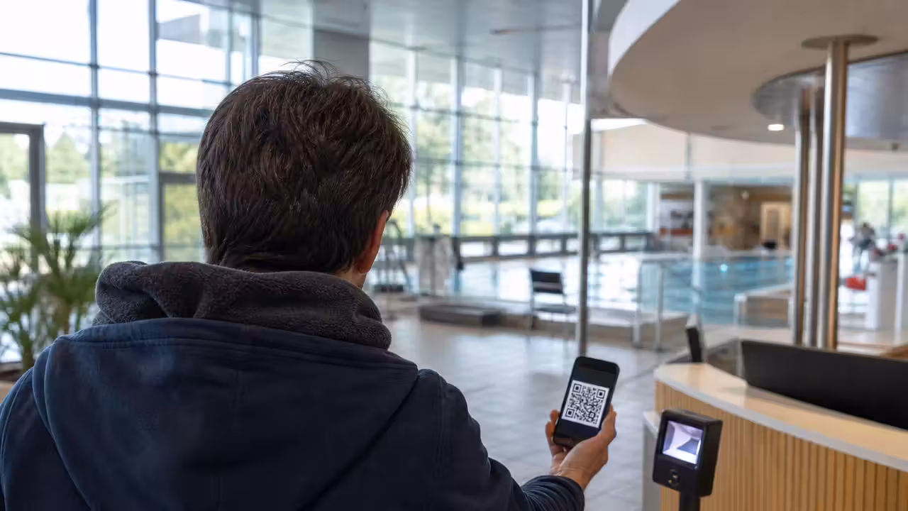 Usagère de dos présentant un QR code sur son téléphone à l’entrée d’un centre aquatique