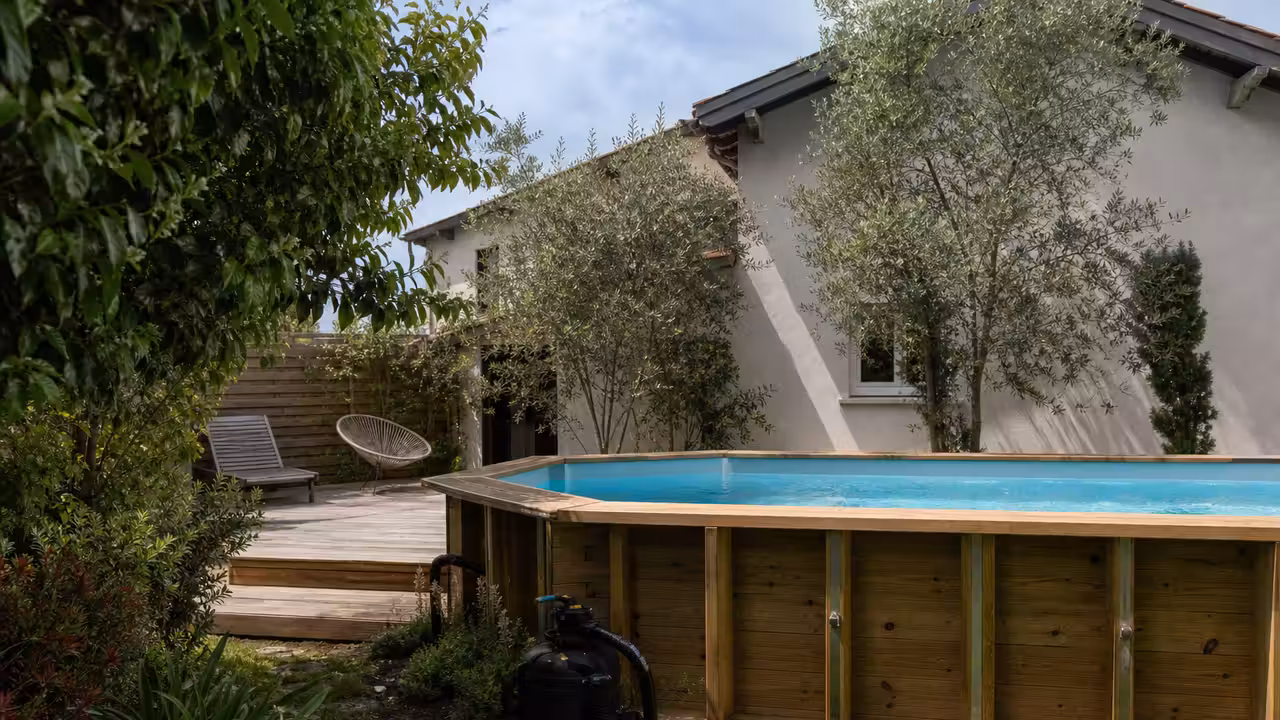 Piscine hors-sol en bois installée dans un jardin avec terrasse et équipement de filtration visibles