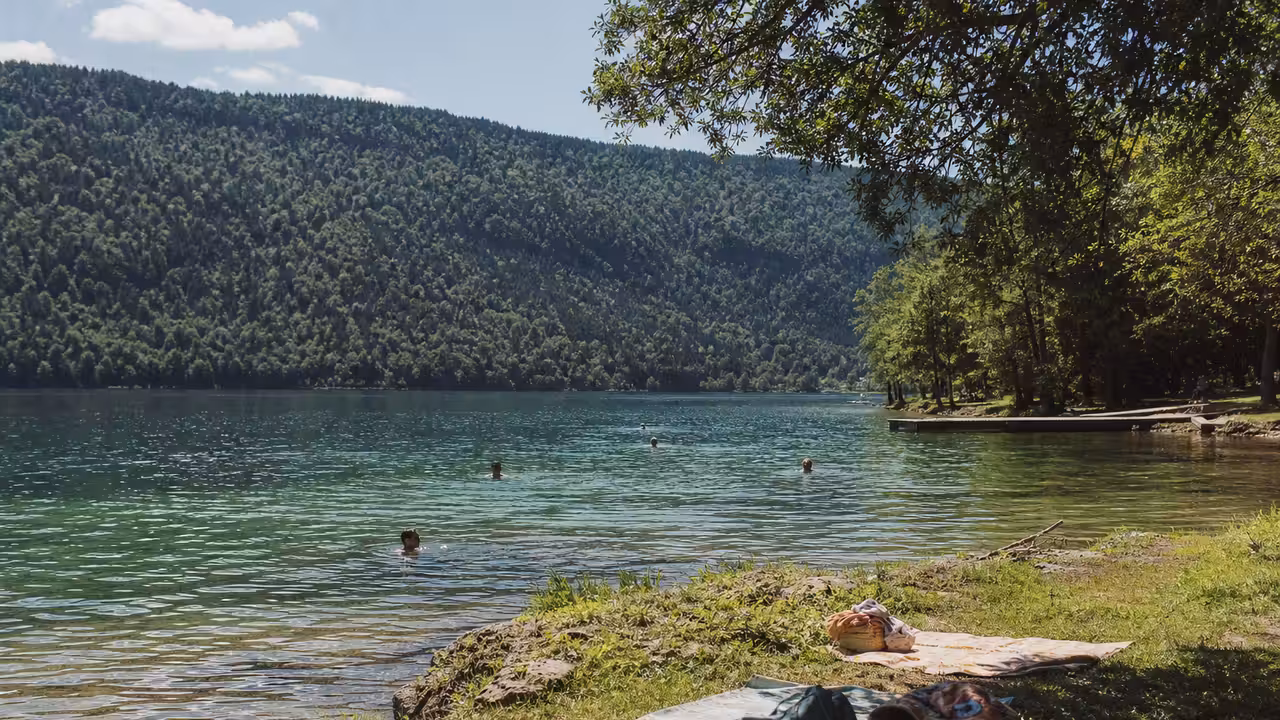 Baigneurs vus de loin au bord d’un lac jurassien, une alternative estivale à la piscine municipale