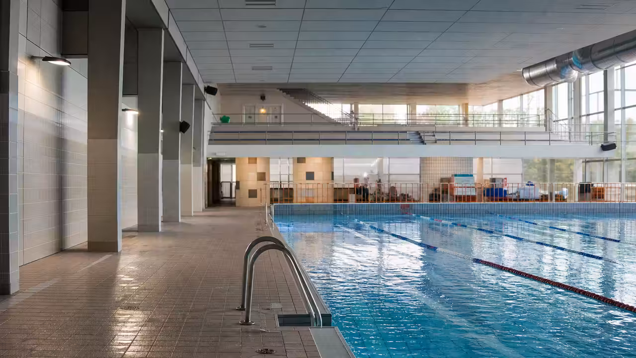 Hall de piscine municipale couvert avec plafond suspendu, baies vitrées et lignes d’eau calmes