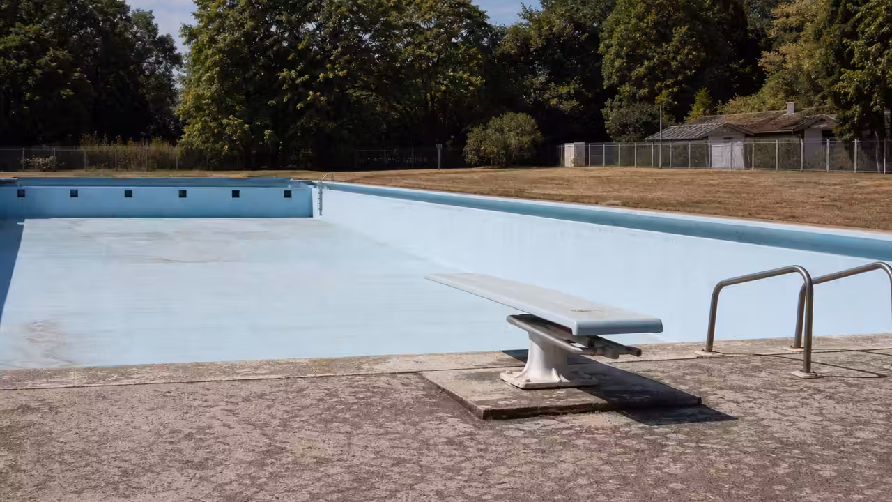 Bassin extérieur municipal vide à la fin de l’été, avec plongeoir et chaises longues autour de l’eau