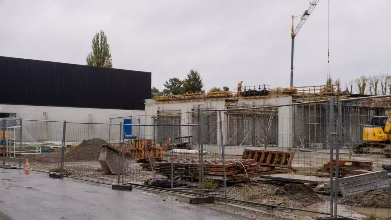 Chantier d’un centre aquatique municipal près d’un gymnase, avec engins et structure en béton