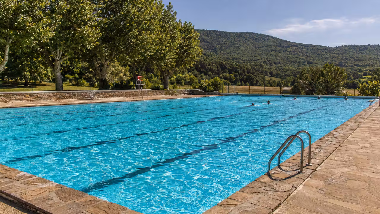 Bassin extérieur de piscine municipale entouré d’arbres, avec lignes d’eau et espace de détente en été