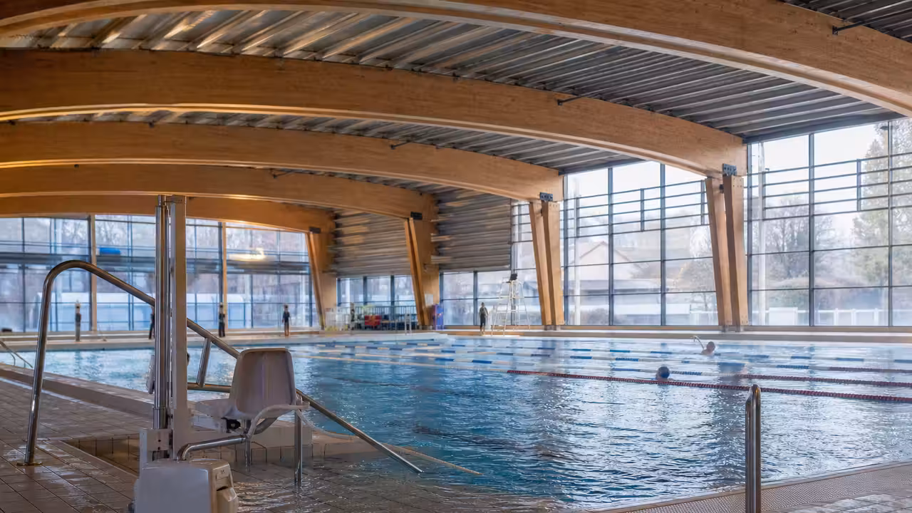 Vue intérieure d’un centre aquatique public moderne avec bassin de nage, baies vitrées et plages accessibles