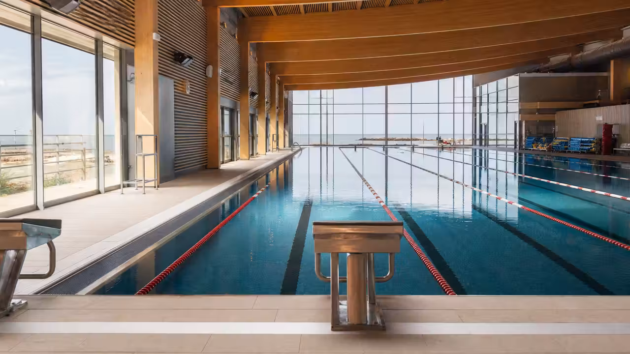 Intérieur lumineux d’un centre aquatique public avec bassin de nage, lignes d’eau et grandes baies vitrées