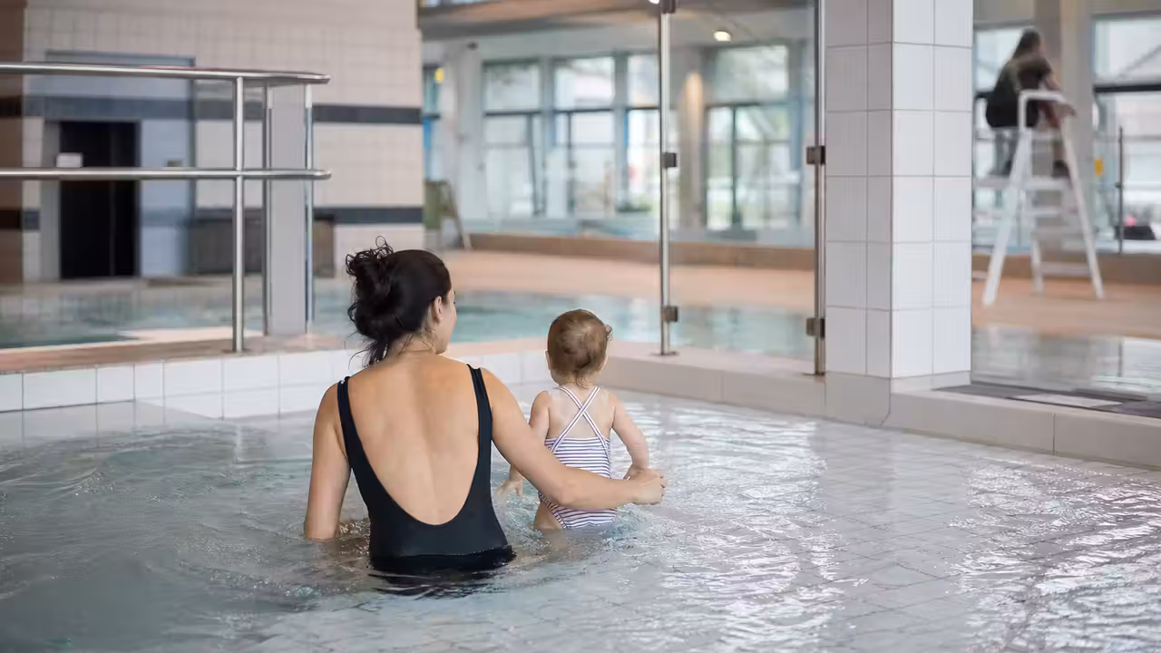 Séance d’éveil aquatique dans un bassin public, avec parent accompagnant un tout-petit près du bord