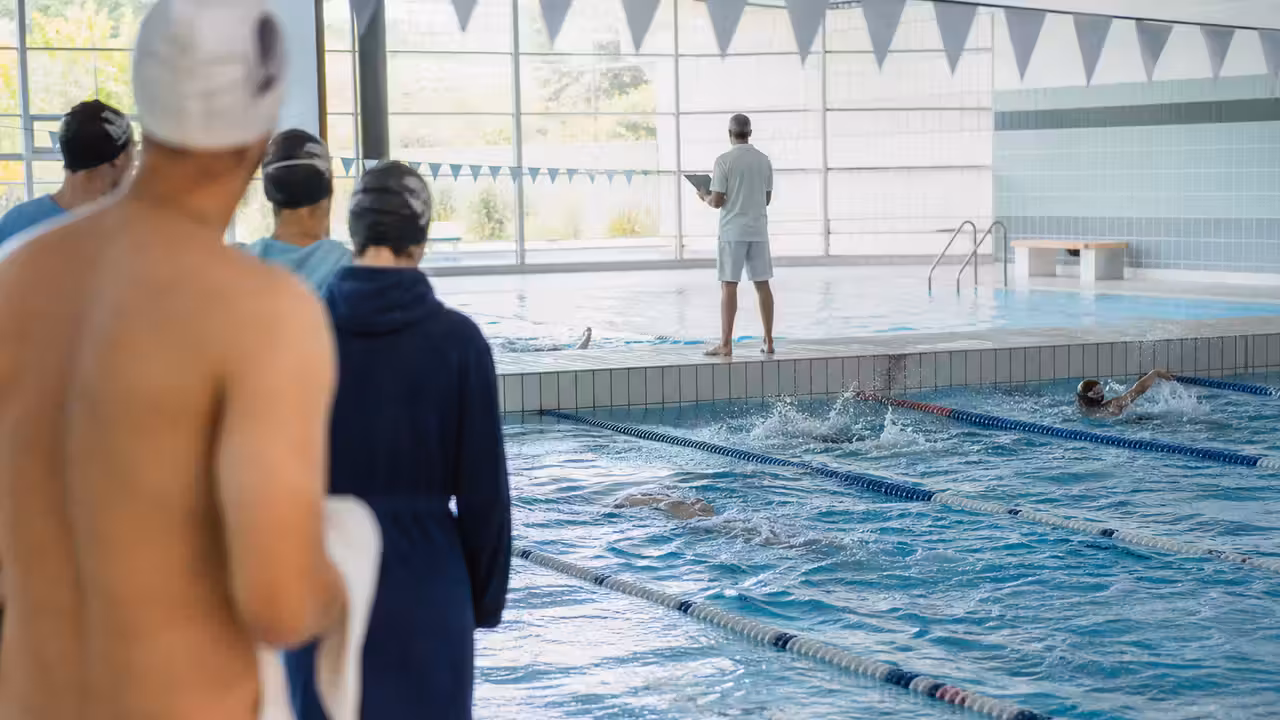 Nageurs adultes se relayant dans les lignes d’eau d’une piscine publique lors d’un défi d’endurance collectif