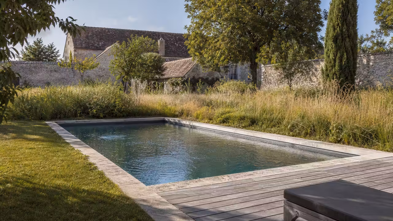 Piscine rectangulaire discrètement intégrée dans le jardin arboré d’une ancienne ferme rénovée