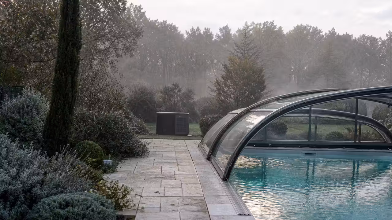 Piscine extérieure couverte par un abri vitré, ouverte sur une terrasse végétalisée par temps frais