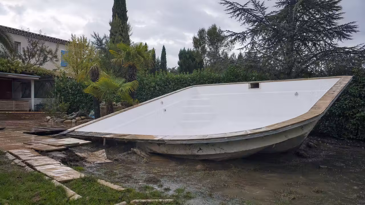 Coque polyester vide soulevée hors du sol dans un jardin détrempé, margelles disloquées après une remontée de nappe