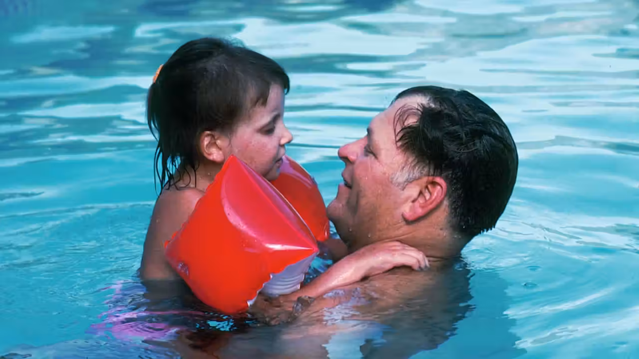 Leçon de natation encadrée dans un bassin couvert, avec enfants vus de dos près du maître-nageur