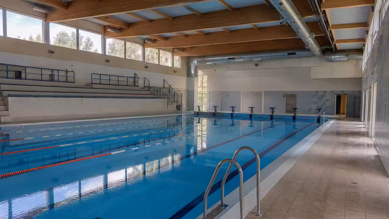 Bassin municipal couvert vide, avec lignes d’eau, gradins sobres et équipements techniques en arrière-plan