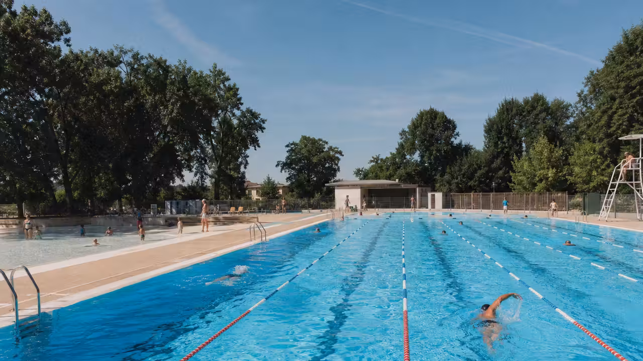 Bassin extérieur d’une piscine municipale animé en été, avec couloirs de nage et espace familial