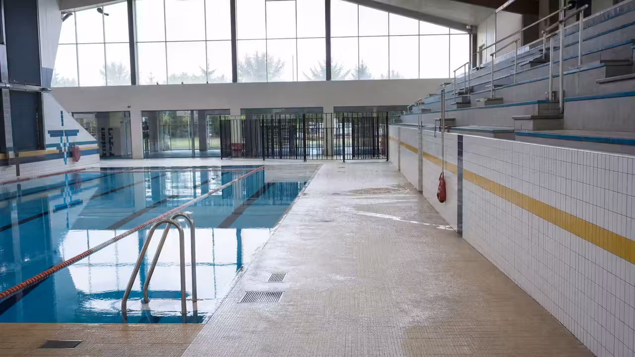 Entrée fermée d’un centre aquatique municipal avec bassin visible derrière les baies vitrées