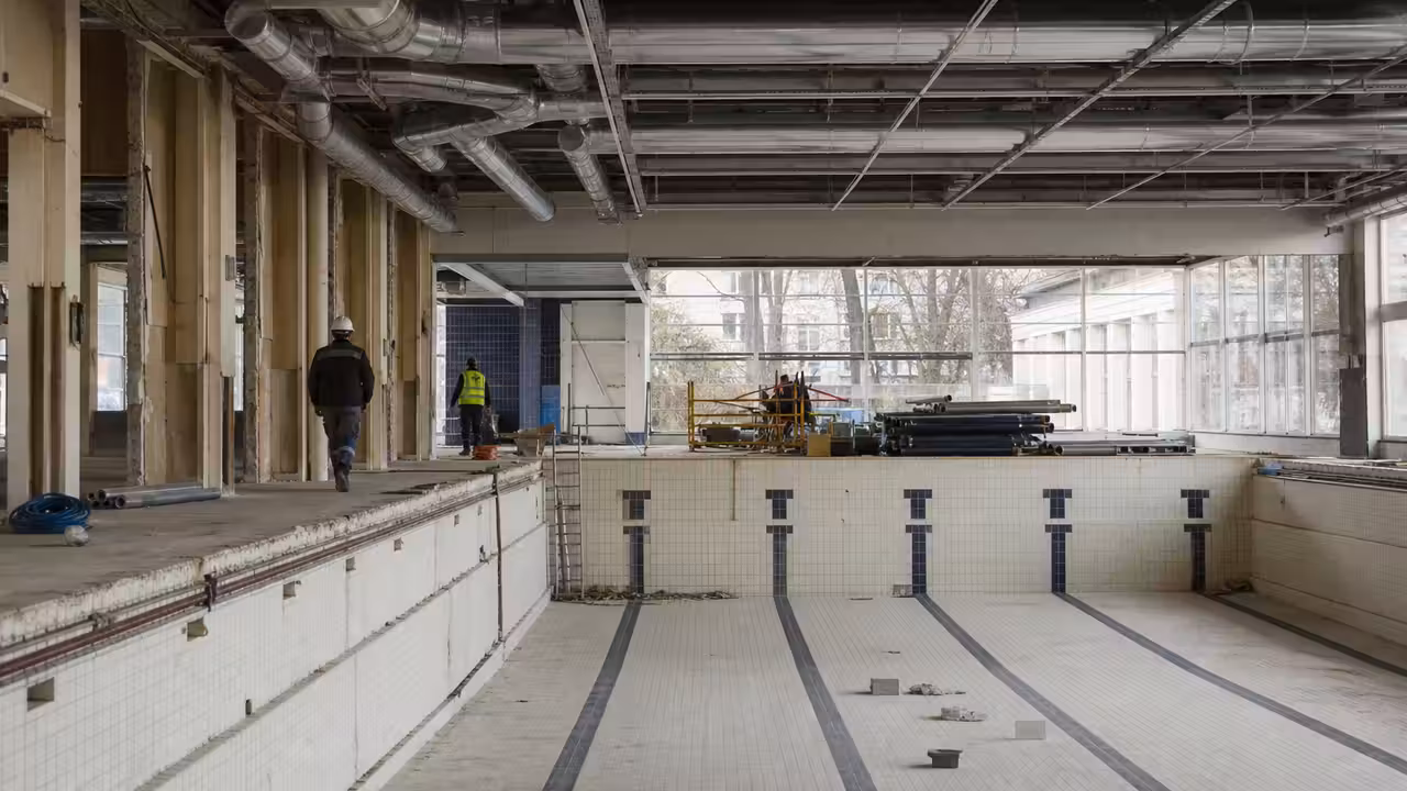 Bassin d’une piscine municipale en rénovation, avec réseaux techniques visibles et lumière naturelle