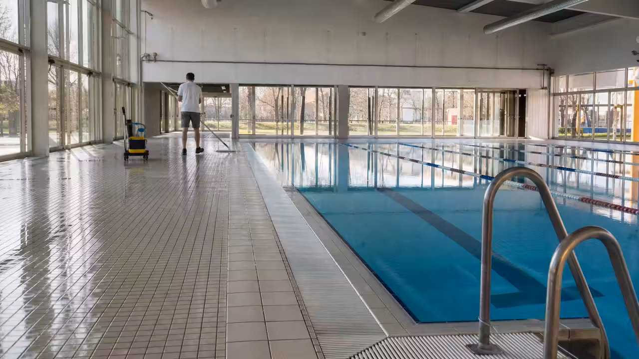 Bassin couvert d’une piscine publique avec lignes d’eau, gradins vides et grandes baies vitrées lumineuses
